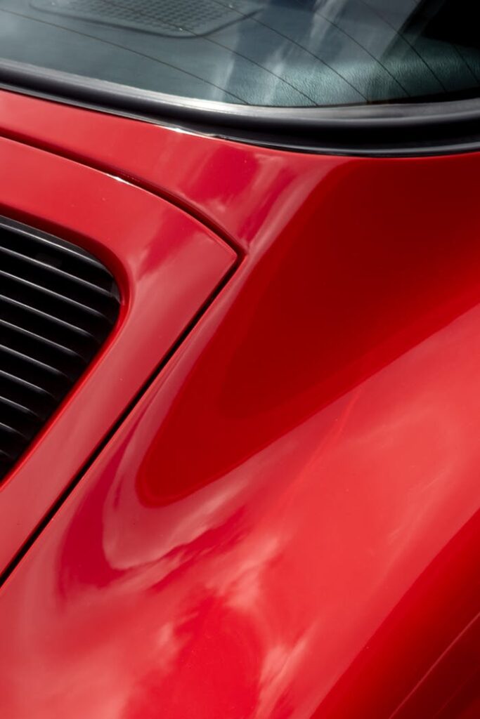 Detailed close-up shot of a red classic car hood showcasing sleek design and curves.